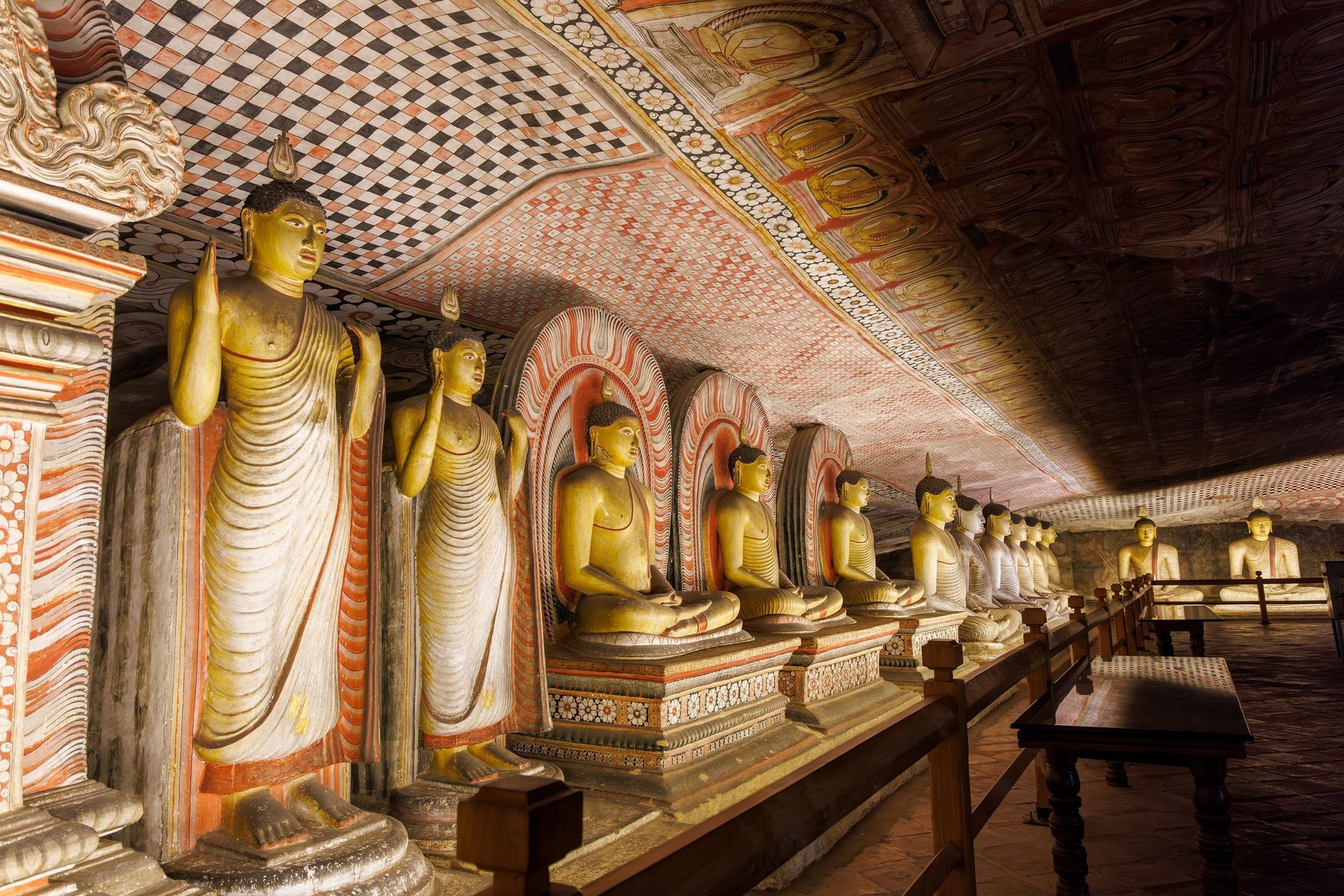 Inside the Dambulla cave temple: a row of standing and seated Buddha statues under a painted rock ceiling