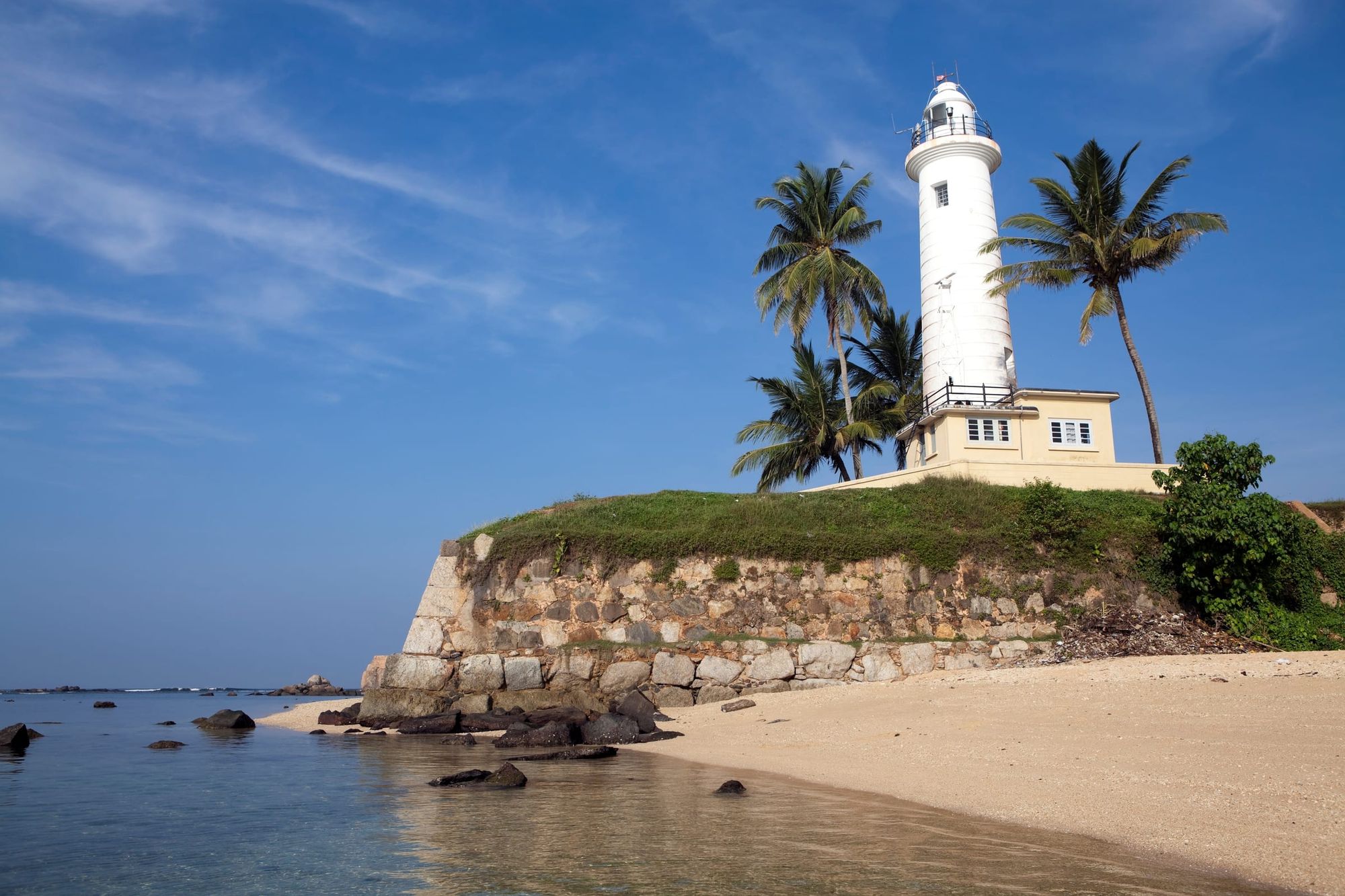 Galle lighthouse on its bastion above a small beach, palms beside it