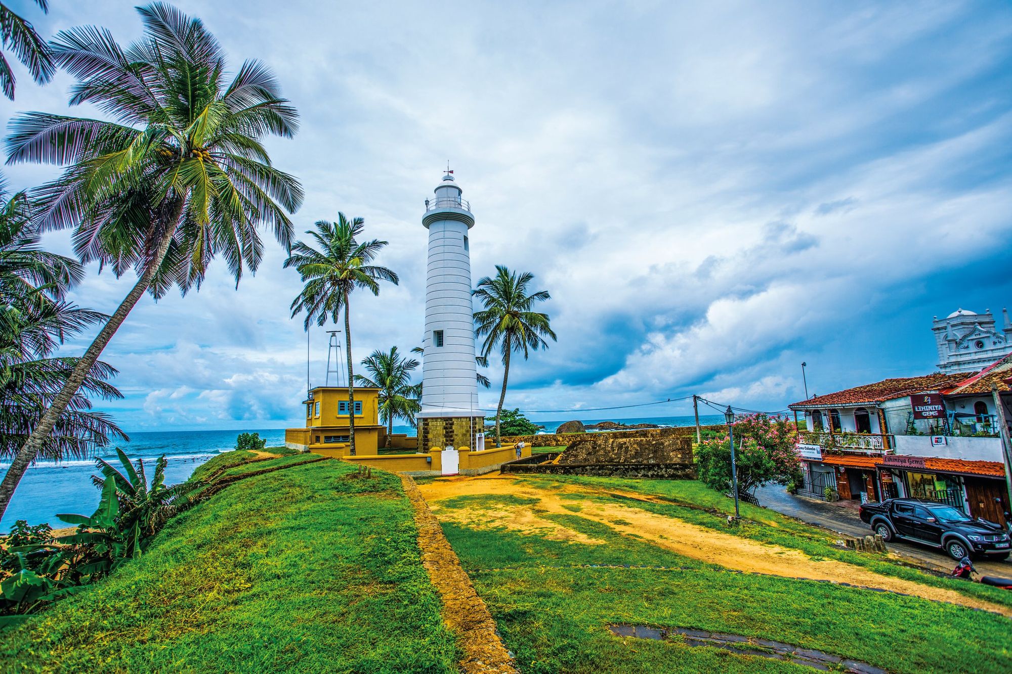Galle lighthouse among palm trees on the fort ramparts, with the sea behind