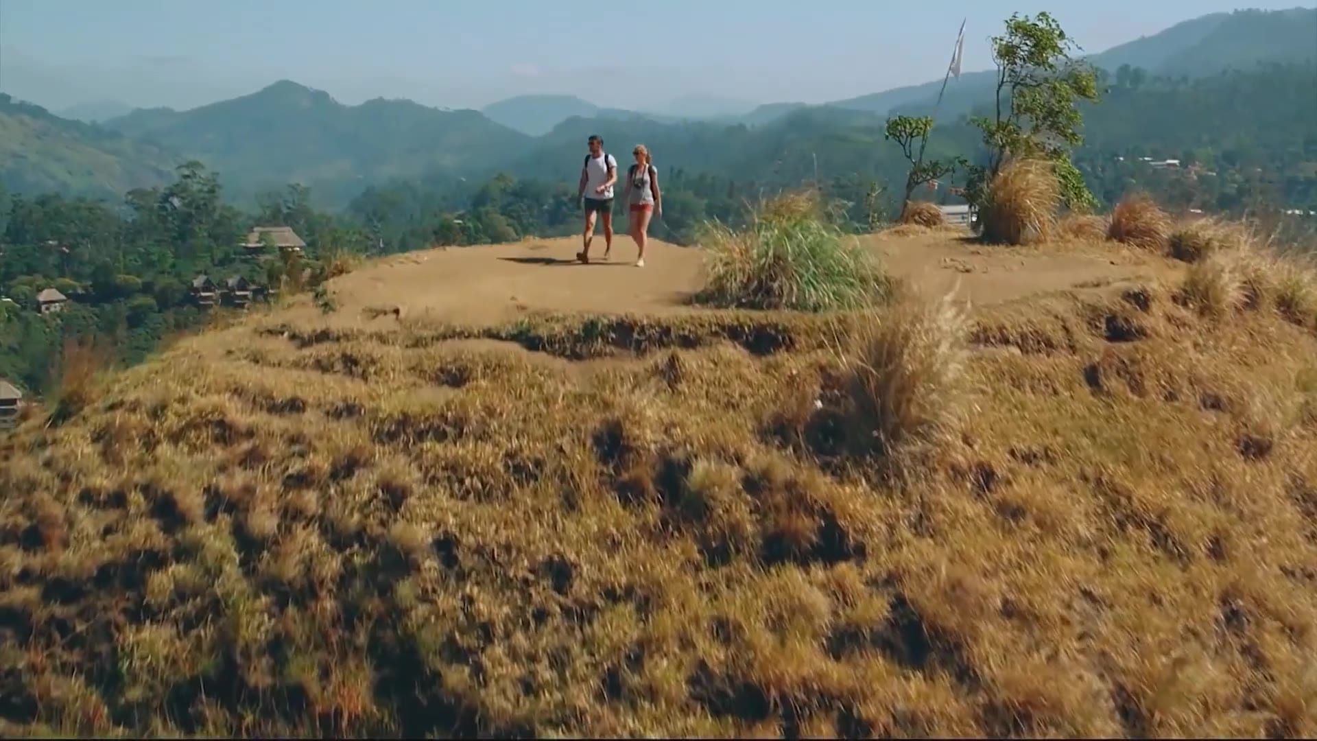 Two walkers on a grassy ridge, green hills behind