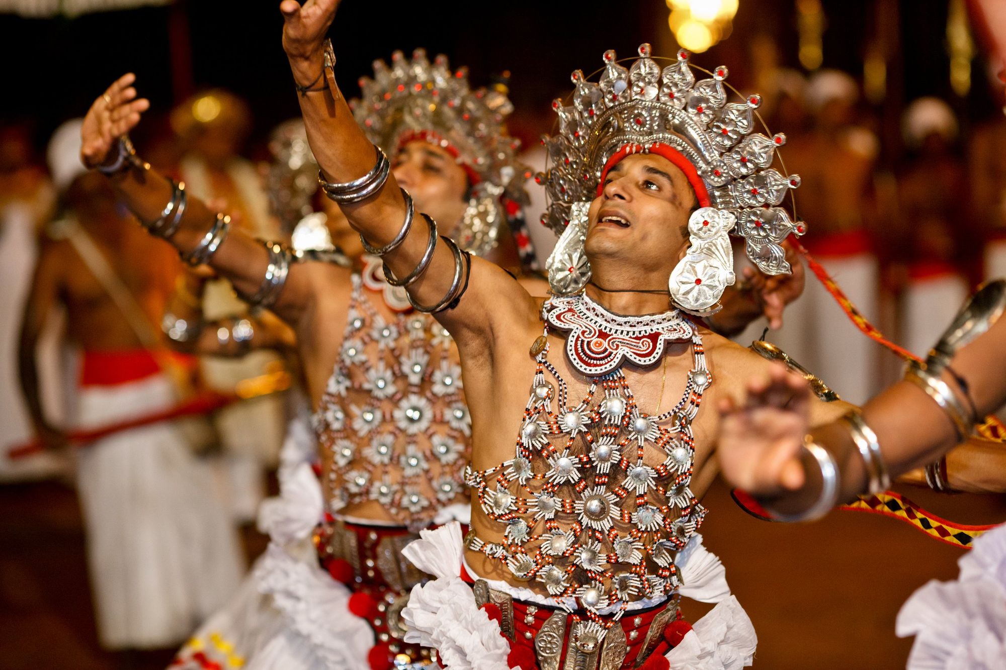A Kandyan dancer in a silver headdress and beaded costume, mid-dance
