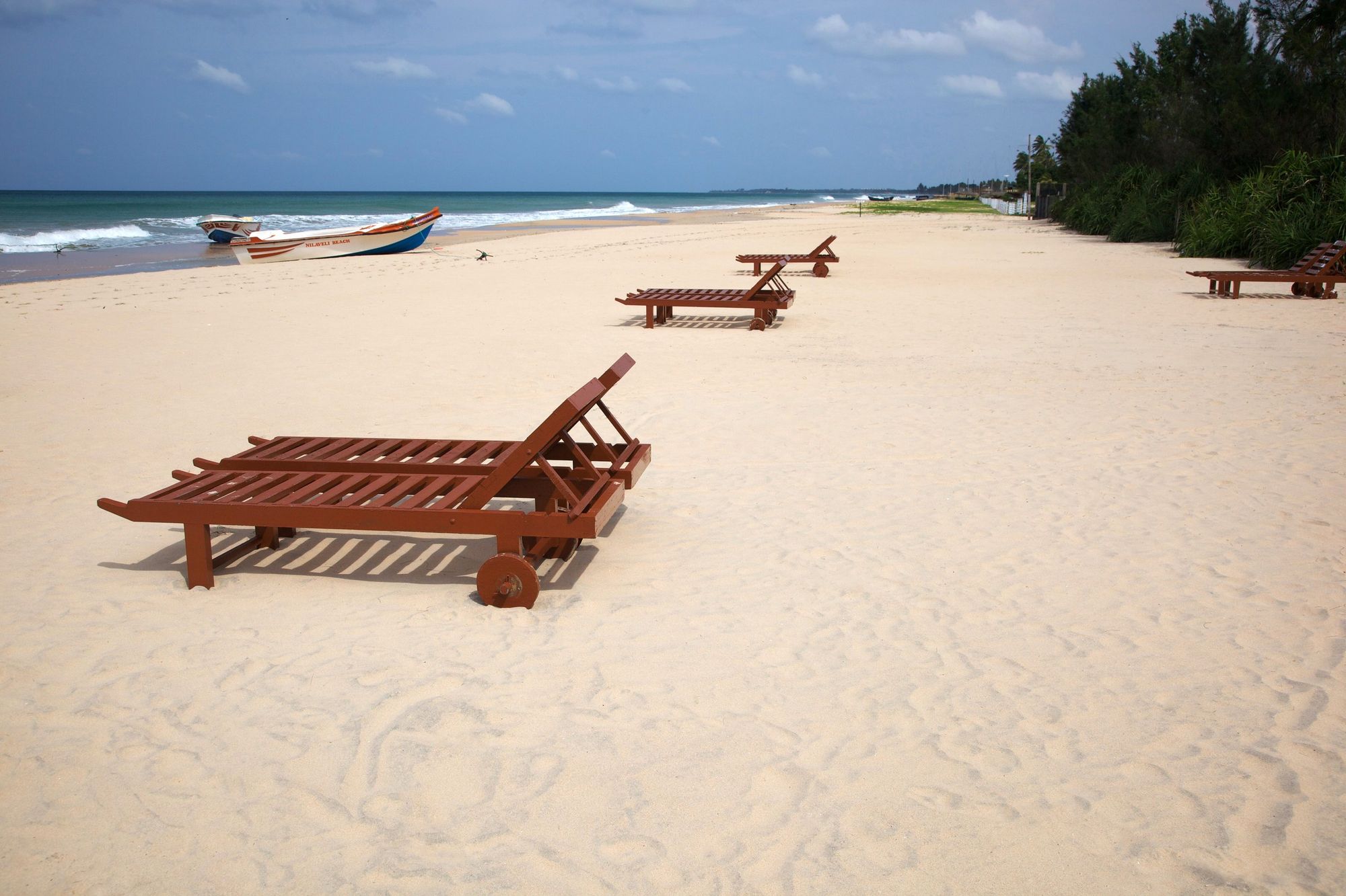 Wooden sun loungers on a wide, empty beach at Nilaveli