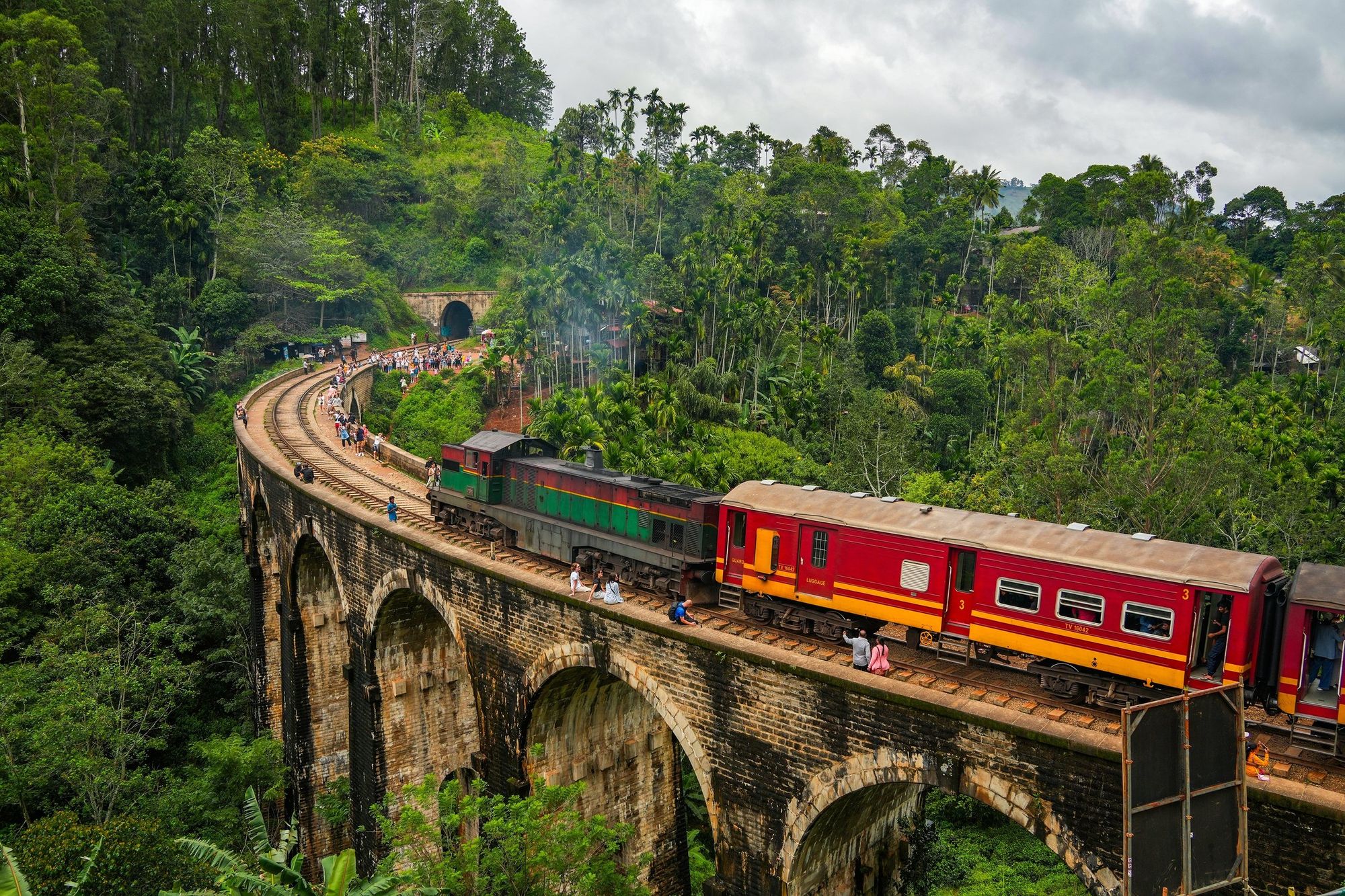A red train crossing the Nine Arch Bridge, with forest close around it
