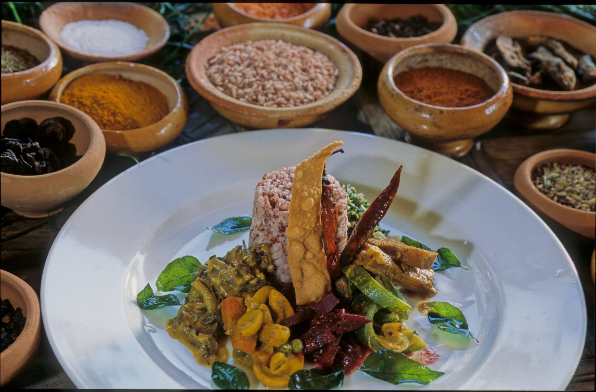 A plate of red rice and curries surrounded by small bowls of spices