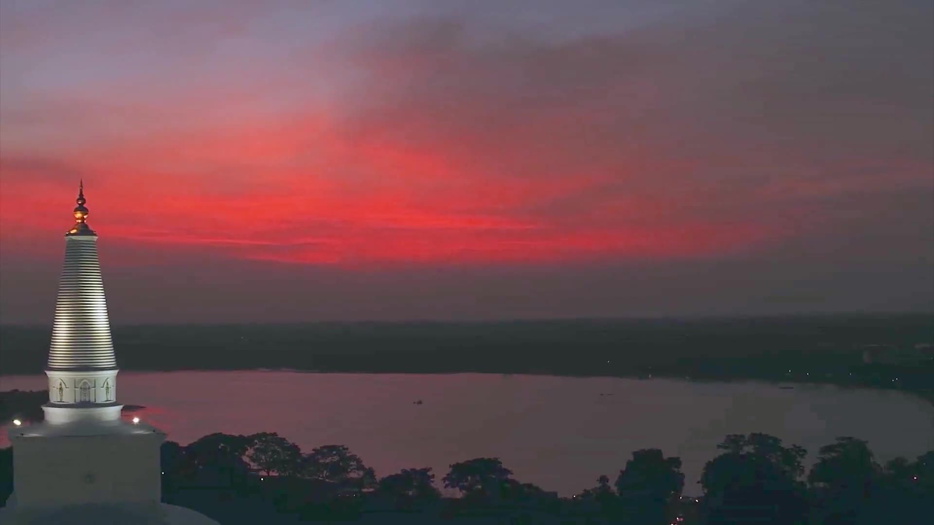 A white stupa beside a lake under a red dusk sky, from the air
