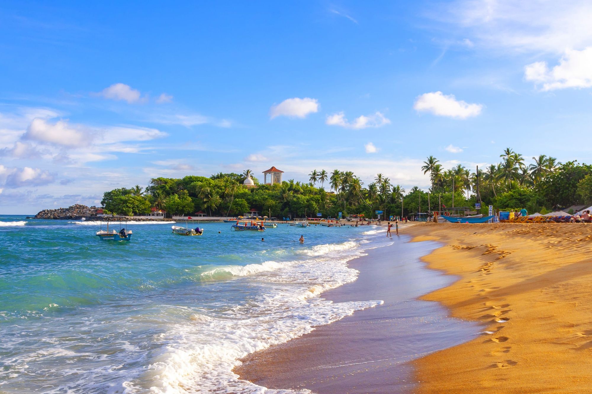 Unawatuna beach: golden sand curving round the bay, small boats in the shallows and palms behind